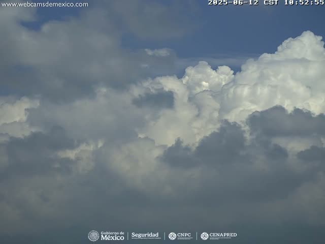 A mostly cloudy sky with large, fluffy cumulus clouds dominates the view.