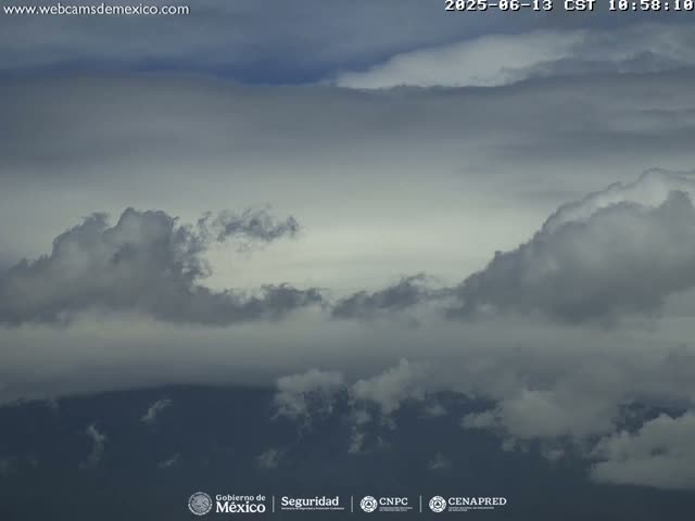 A mostly cloudy sky with dark gray and white cumulus clouds over a dark mountain range.