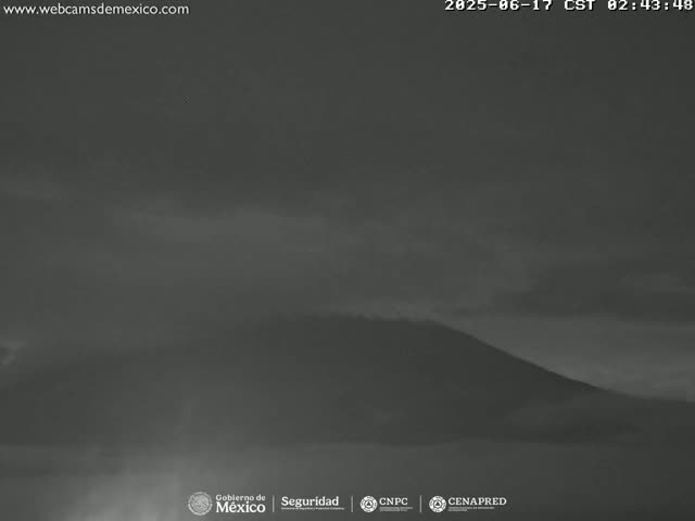 A dark, possibly pre-dawn or early morning, view shows a low-lying mountain shrouded in mist or fog.