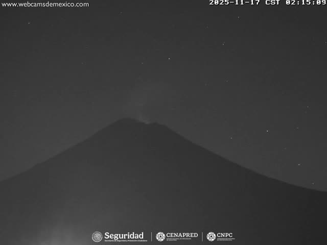 A dark, monochromatic view captures a volcano actively emitting a plume from its summit under a clear night sky with visible stars.