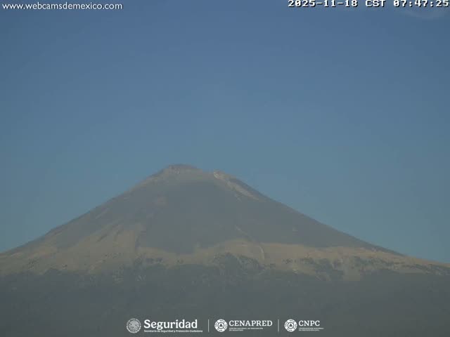 A dark, monochromatic view captures a volcano actively emitting a plume from its summit under a clear night sky with visible stars.