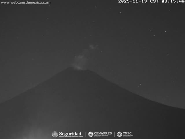 A grayscale nighttime image captures a volcano actively emitting a plume of smoke from its summit under a clear, star-filled sky.