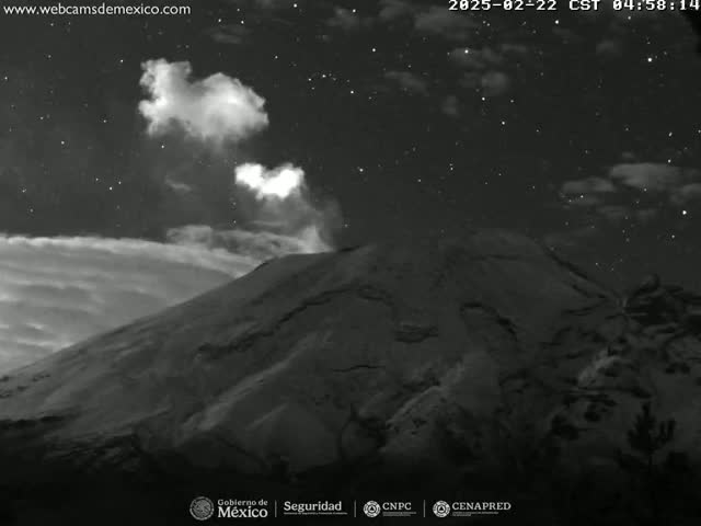 A nighttime, grayscale image shows a volcano emitting a plume of smoke or ash under a starry sky.