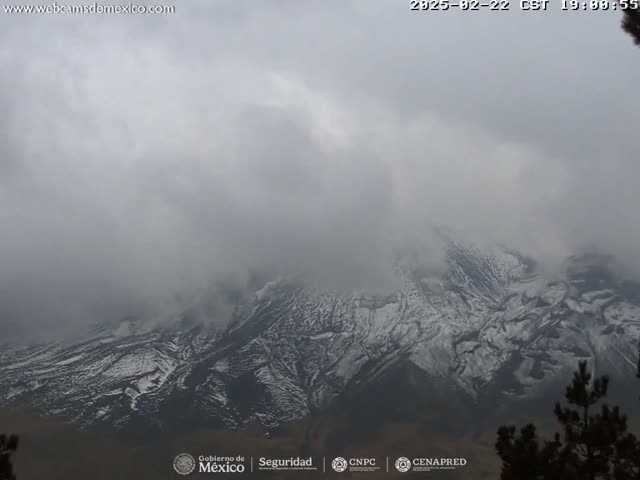 A snow-dusted mountain range is mostly obscured by a thick, gray fog.