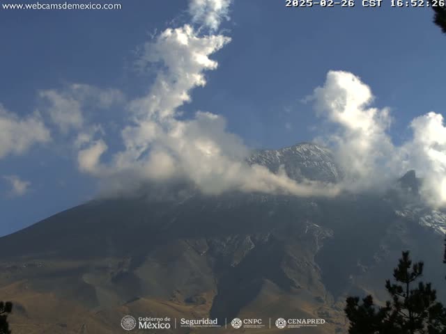 A partially cloudy sky overlooks a large, dark mountain with a dusting of snow near its peak.