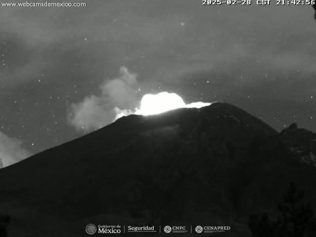 A nighttime, black and white image shows a volcano erupting under a starry sky.