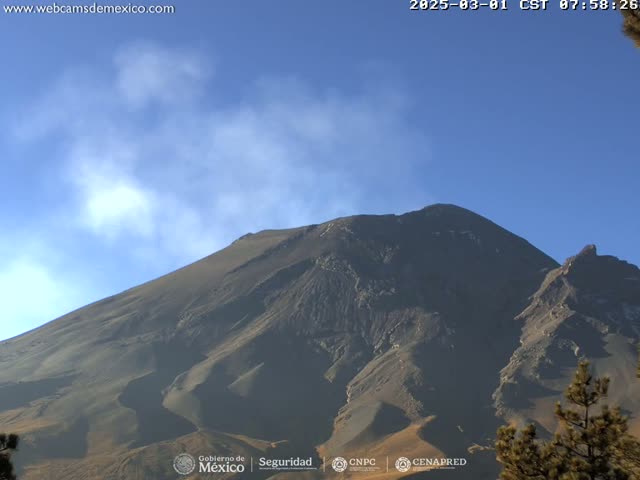 A large, dark-colored mountain with a plume of light smoke is visible under a clear, mostly blue sky.