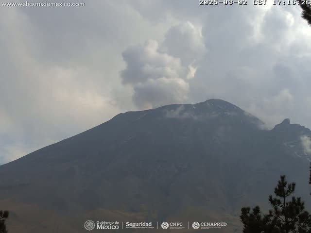 A large, dark mountain with a plume of smoke or clouds rising from its peak is visible under a mostly cloudy sky.