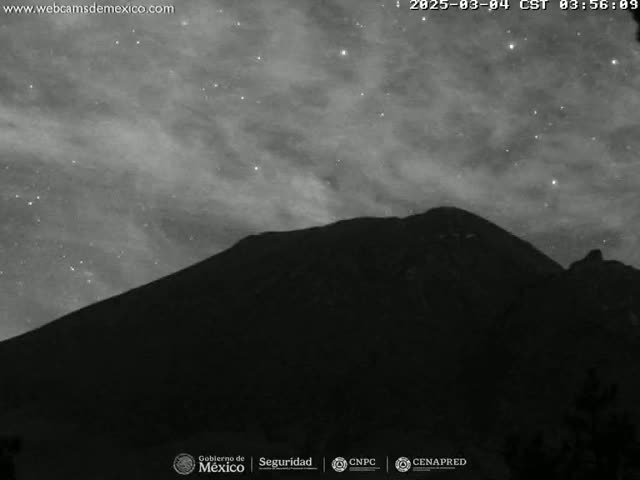 A dark, silhouetted mountain is seen under a night sky with a cloudy, starry expanse.