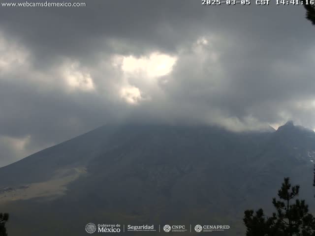 A large, dark mountain is partially obscured by a mostly cloudy sky with breaks of sunlight.