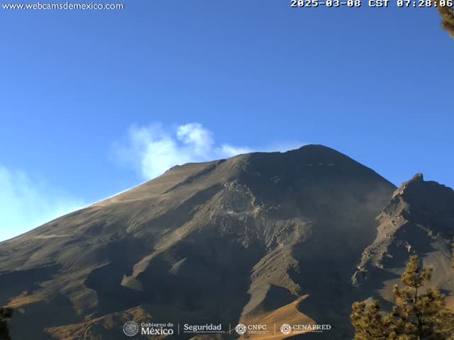 A dark-colored volcanic mountain with a plume of smoke or steam rising from its peak under a clear blue sky.