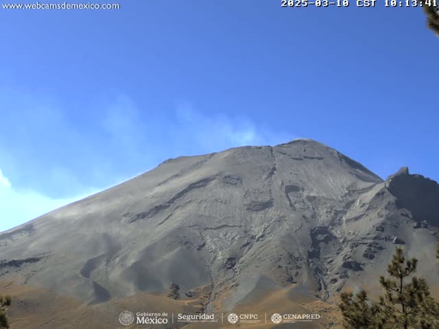A large, dark gray volcanic mountain is visible under a clear blue sky, with a small plume of smoke or ash emanating from its peak.