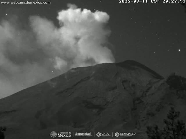 A nighttime, grayscale image shows a volcano emitting a plume of smoke under a starry sky.
