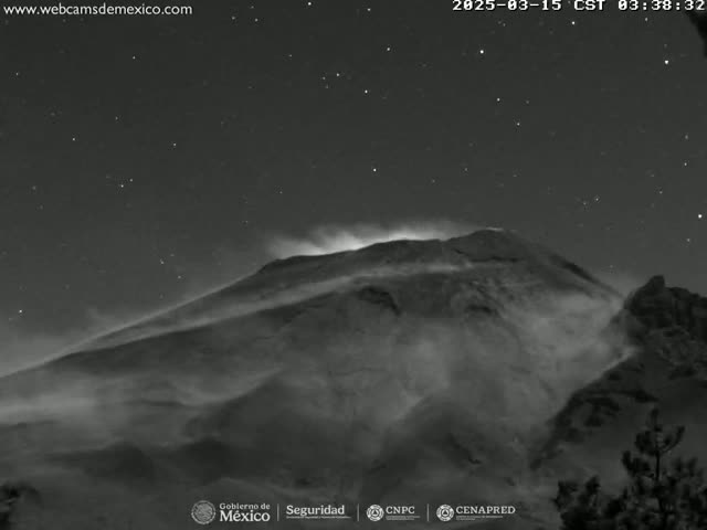 A nighttime, grayscale image shows a volcano emitting smoke or ash under a starry sky.