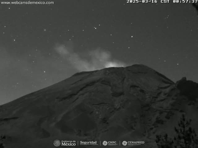 A nighttime, low-light image shows a volcano emitting smoke under a clear, starry sky.