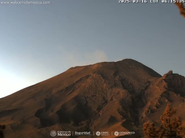 A large, dark brown volcanic mountain is seen under a clear, light blue sky.
