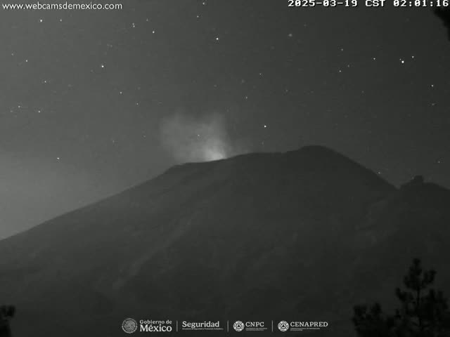 A nighttime, low-light image shows a volcano emitting a faint plume of smoke under a starry sky.