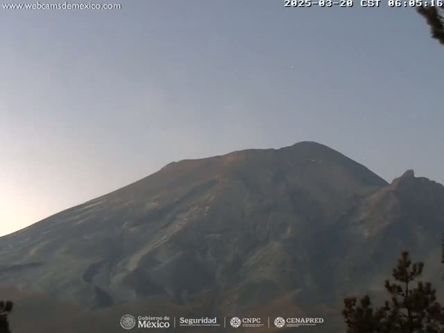 A large, dark-colored mountain is seen under a pale, clear sky.