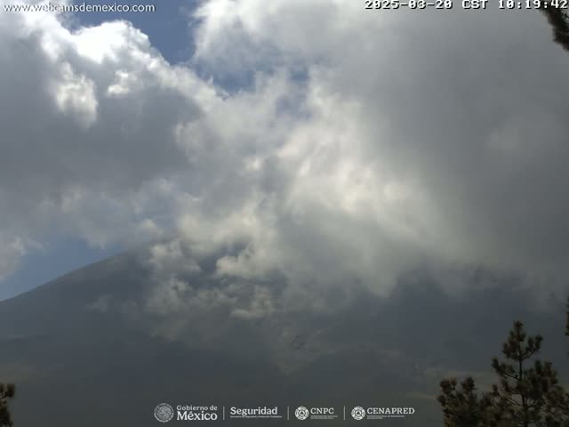 A large mountain is partially obscured by a mostly cloudy sky, with some sunbeams breaking through the clouds.