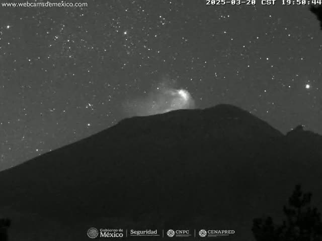 A dark mountain is silhouetted against a night sky filled with stars, and a faint glow emanates from near its peak.