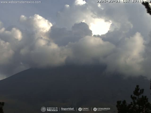 A partly sunny sky with fluffy clouds hangs over a dark mountain range, partially obscured by the cloud cover.