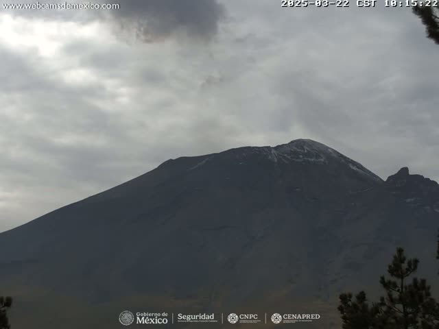 A large, dark mountain with a dusting of snow on its peak is visible under an overcast sky.