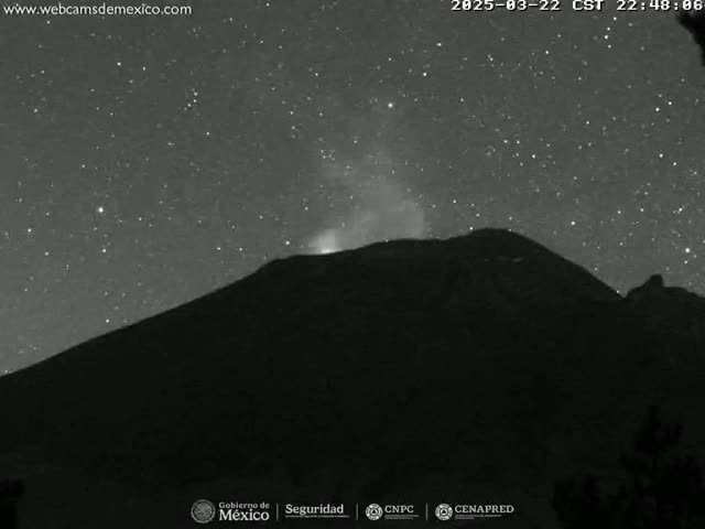 A dark mountain silhouetted against a night sky filled with stars, with a faint glow emanating from its peak.