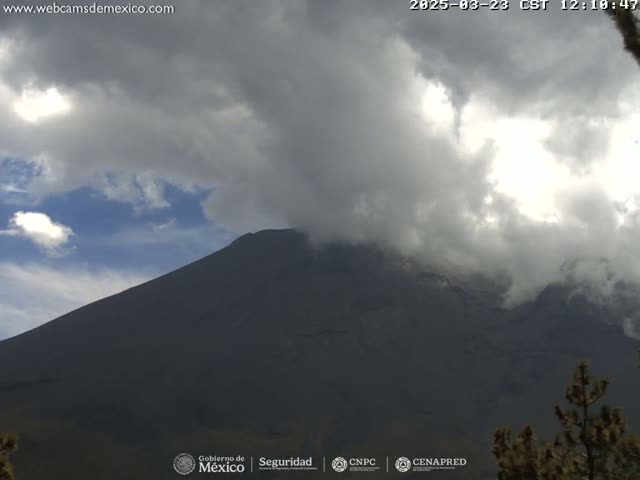 A dark, large mountain is partially obscured by a cloudy sky with patches of blue visible.