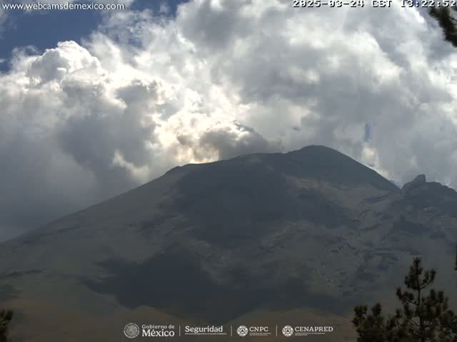 A large, dark mountain is partially obscured by a cloudy sky with some sunlight breaking through.