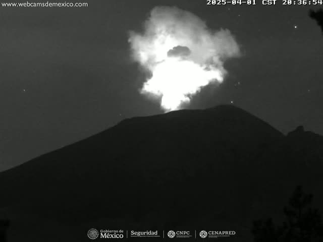 A nighttime, black and white image shows a volcano erupting, emitting a bright plume of smoke and ash against a dark, starry sky.