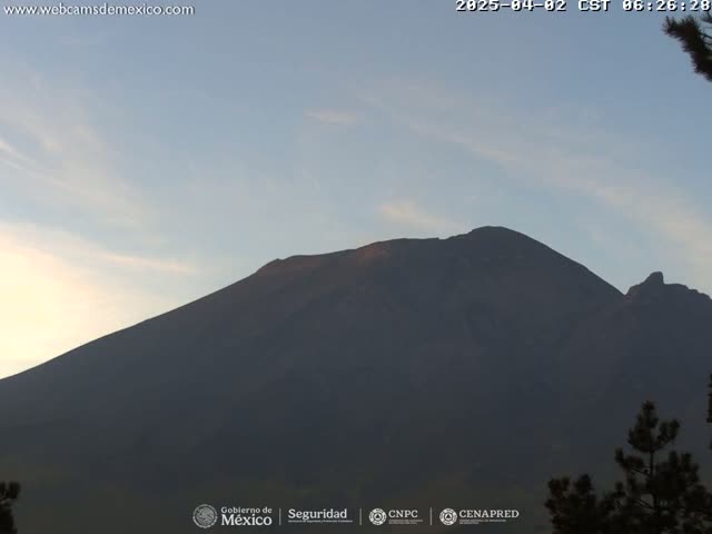 A large, dark mountain is visible against a pale, clear sky at dawn.