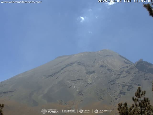 A large, dark-grey volcanic mountain is visible under a mostly clear, light-blue sky with a few small clouds.