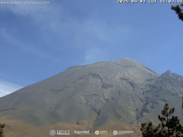 A large, gray volcano is seen under a clear, mostly blue sky.