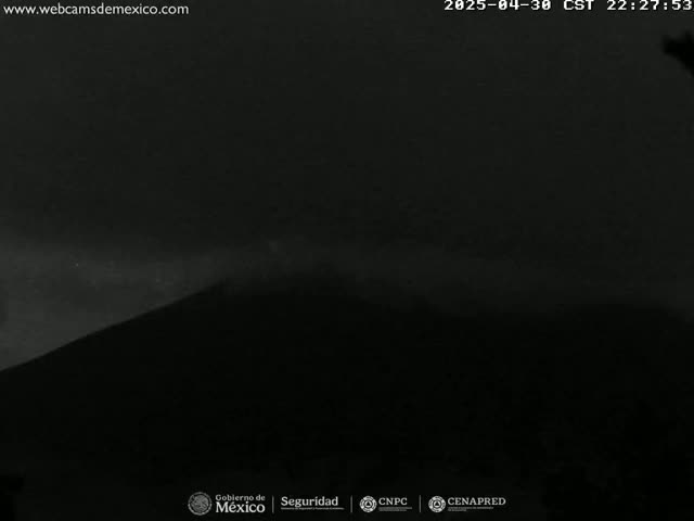 A dark, silhouetted hill is visible under a mostly clear night sky.