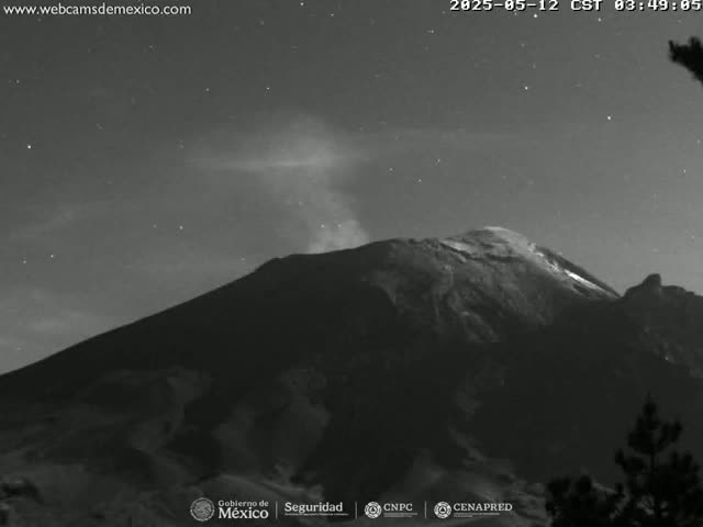 A grayscale nighttime image shows a volcano emitting a plume of smoke under a clear, starry sky.