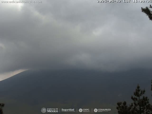 A dark, overcast sky hangs over a distant, shadowy mountain range, with a few trees visible in the lower right corner.