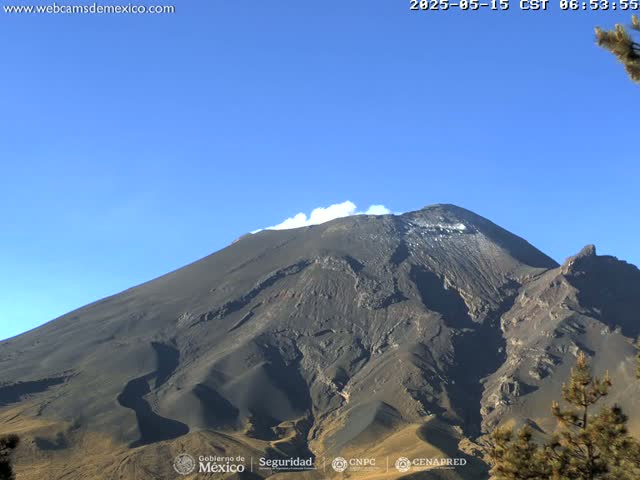 A large, dark-colored volcano with a small amount of snow near the summit is visible under a clear blue sky.