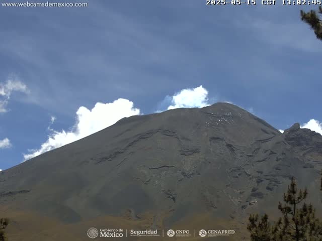 A large, dark gray volcano is visible under a mostly clear blue sky with some scattered white clouds.