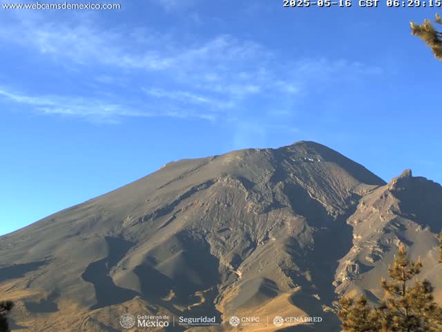 A large, dark-colored mountain is seen under a mostly clear, bright blue sky.