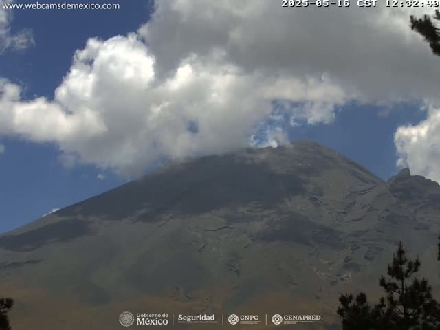 A large, dark-grey mountain is partially obscured by fluffy white clouds under a mostly blue sky.