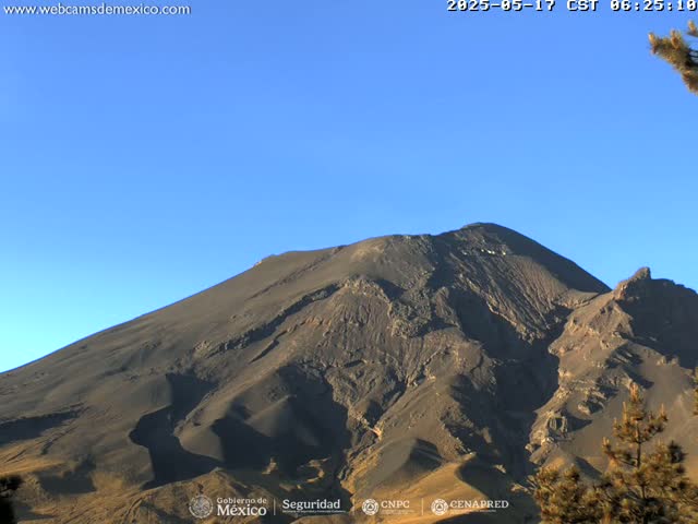 A large, dark-colored mountain is shown under a clear blue sky.