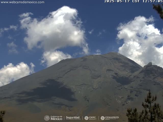 A large, dark-grey mountain is visible under a mostly sunny sky with scattered cumulus clouds.