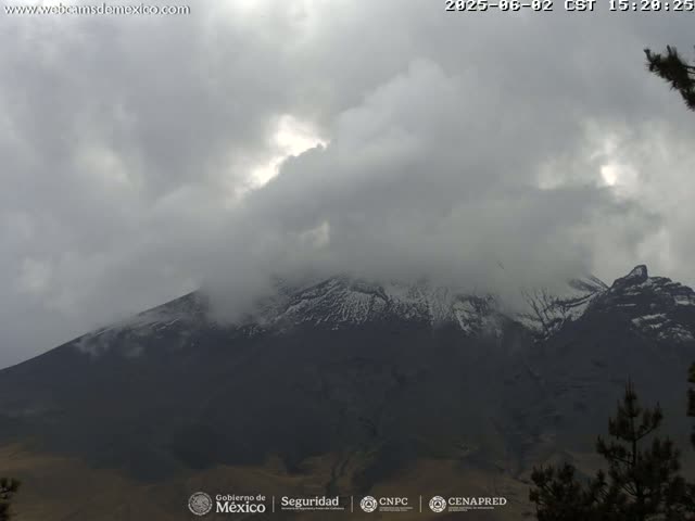 A snow-capped mountain is partially obscured by a cloudy, overcast sky.