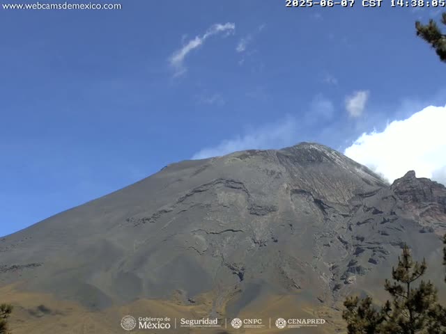 A large, gray volcanic mountain is visible under a mostly clear blue sky with a few scattered clouds.