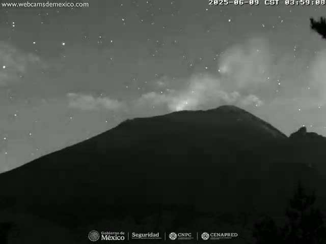 A dark, silhouetted mountain is seen at night under a starry sky with some clouds and a plume of smoke or ash rising from its peak.