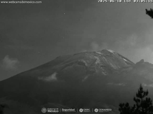A nighttime, low-light grayscale image shows a large, dark mountain with a slight haze or smoke emanating from its peak, under a mostly clear sky.