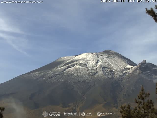 A snow-capped mountain is seen under a mostly clear blue sky.