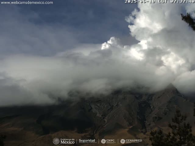A large, mountainous landscape is shrouded in thick, grey clouds under a partly cloudy sky.