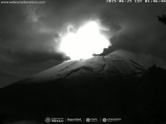 A brightly lit volcanic eruption is seen at night against a dark, cloudy sky.