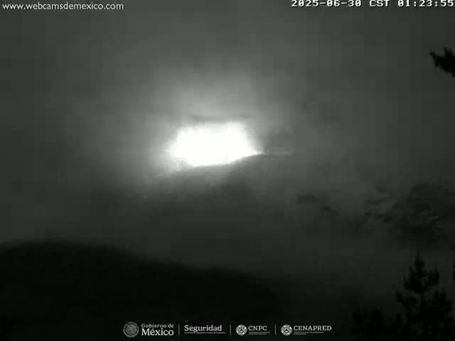 A bright light shines through a hazy, dark sky over a mountain range.